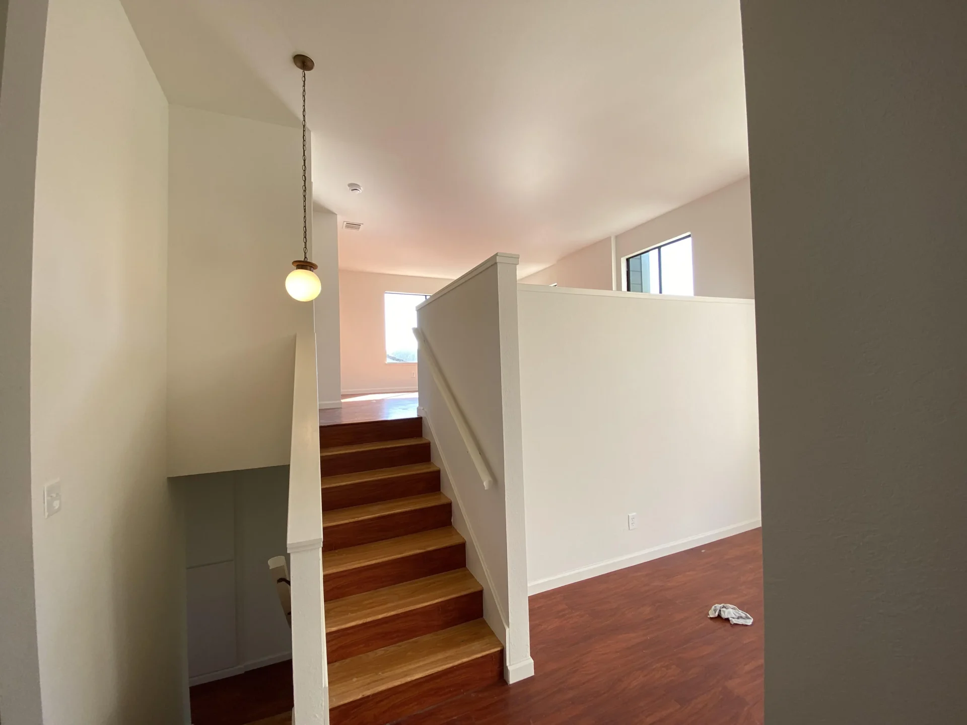 A staircase with wooden steps and white railing leads to an upper floor with hardwood flooring, a hanging light fixture, and a window allowing natural light into the space. interior painting company